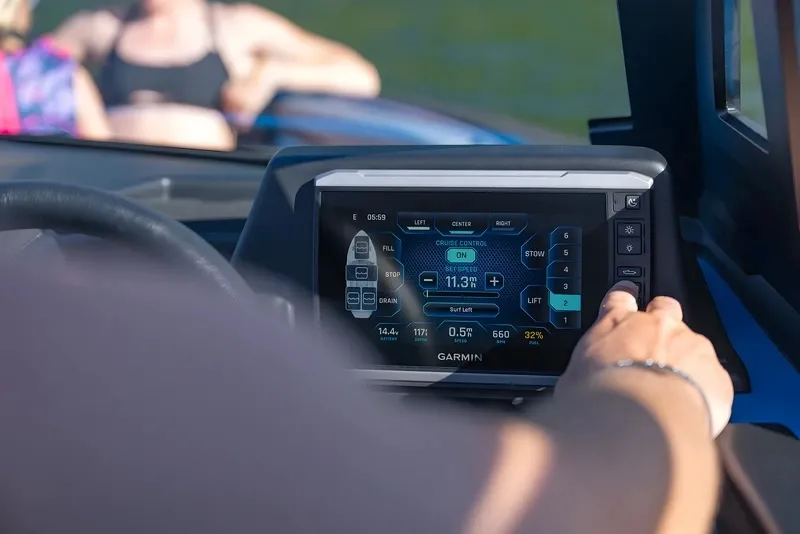Close-up of a hand adjusting the Garmin touchscreen on the Axis Dash, showing speed and ballast controls, with passengers blurred behind.