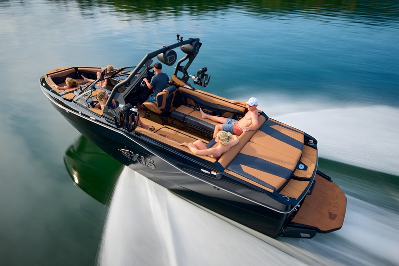 A black Axis T235 with tan interior runs at speed across a lake, a full crew aboard and forested shore blurring past.