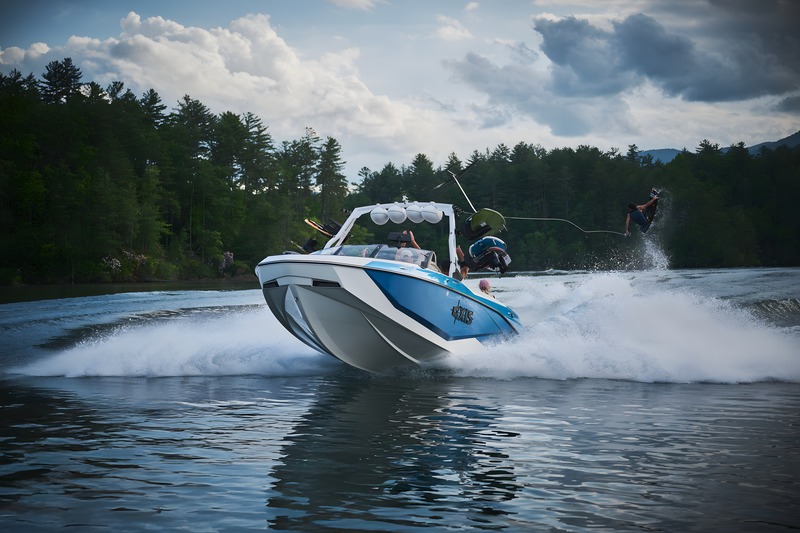 Seen head-on, a white-and-blue Axis wake boat charges forward as a wakeboarder catches air behind under a dramatic cloudy sky.