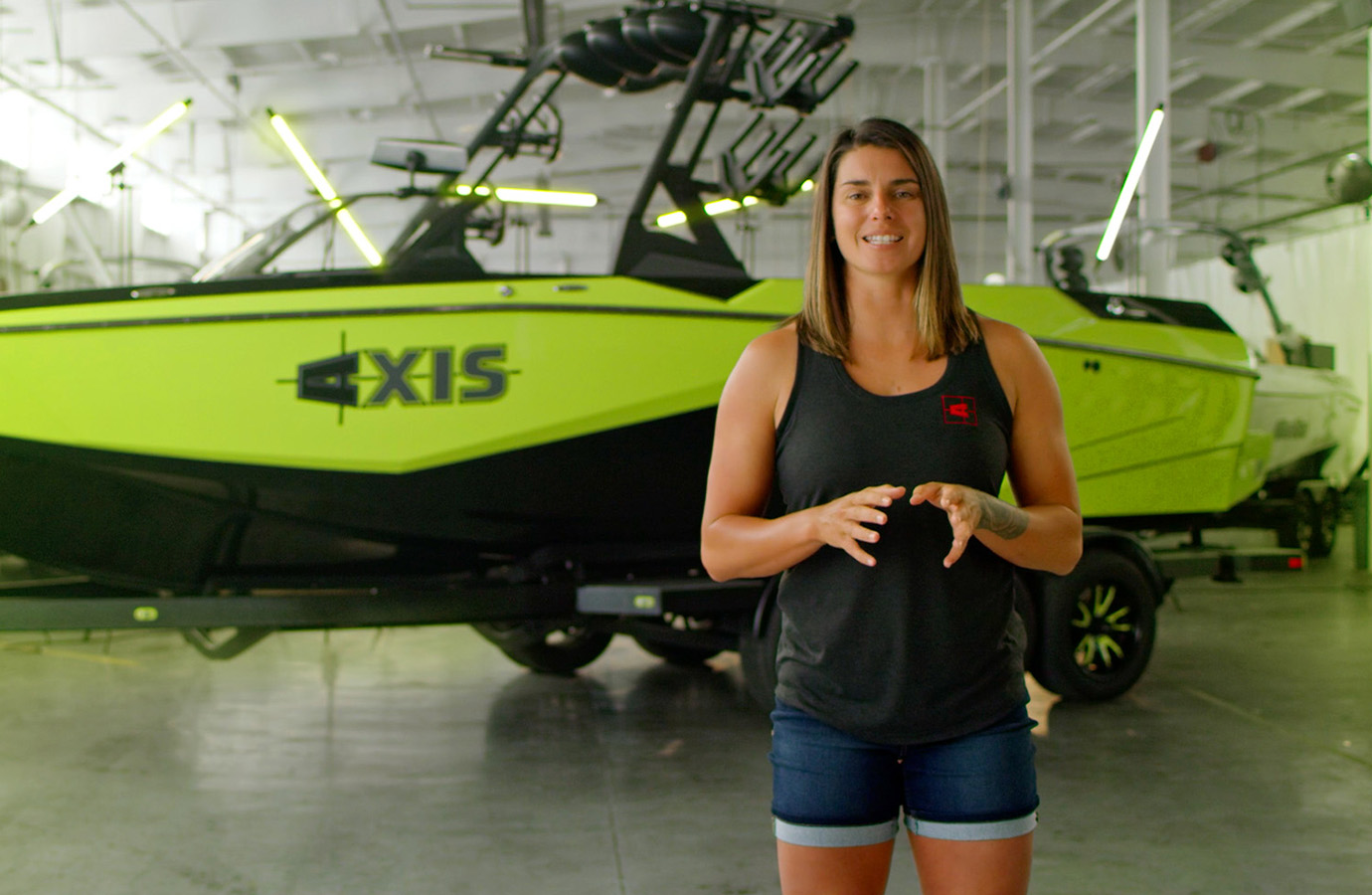 Axis pro athlete Bec Gange speaks to camera in a warehouse, a lime green and black Axis A245 on its trailer lit by green accent lights.