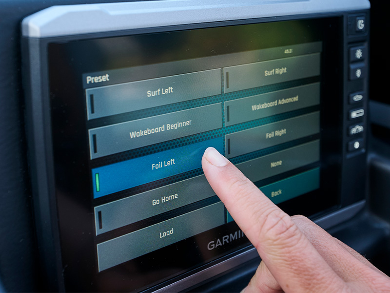 A finger taps the Foil Left preset on the Axis Garmin touchscreen, which lists surf, wakeboard, and foil ride-setting presets for the boat.