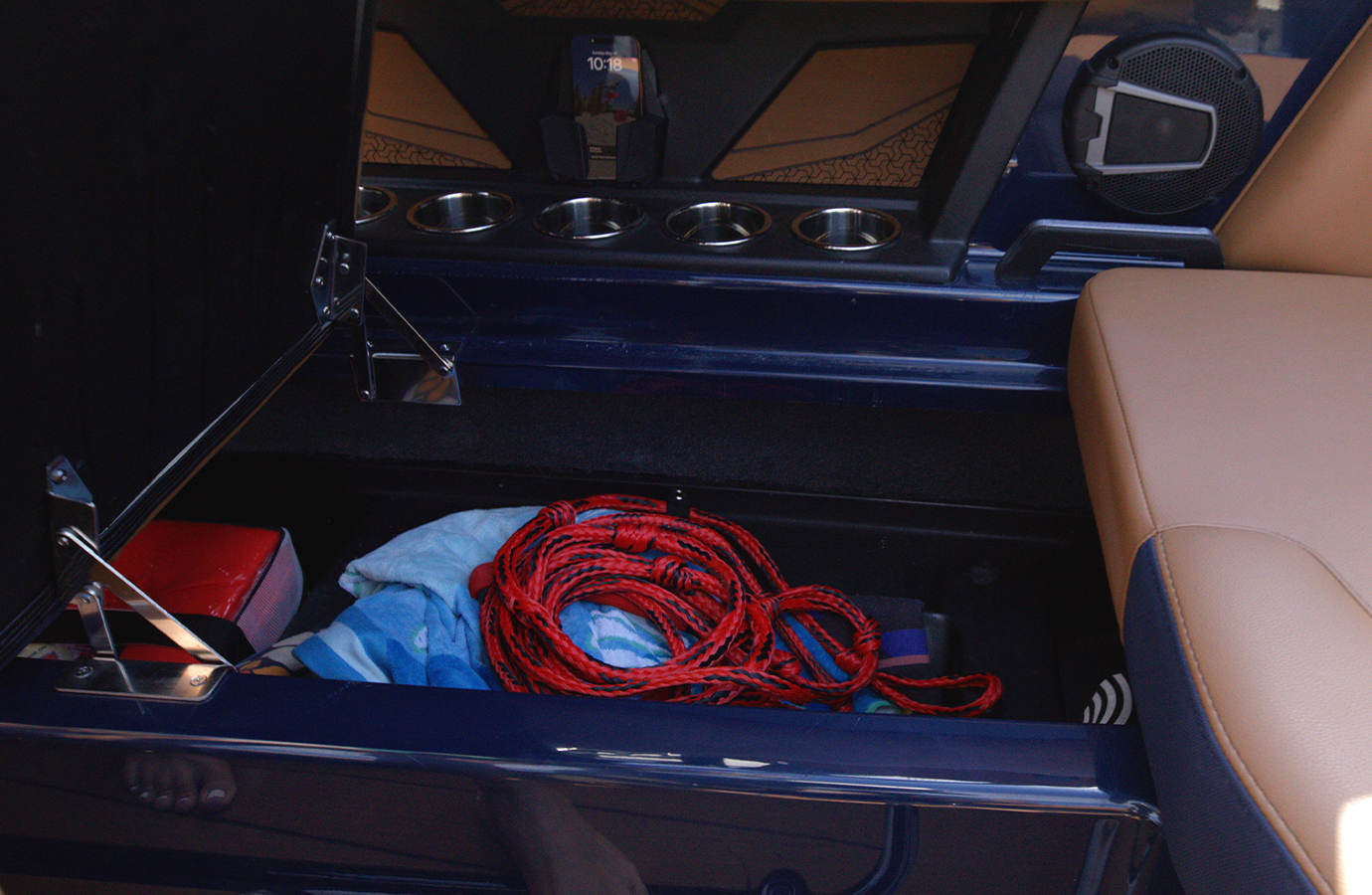An open under-seat storage compartment in an Axis A-Series holds a coiled red tow rope, towels and gear, with tan seating and cupholders above.