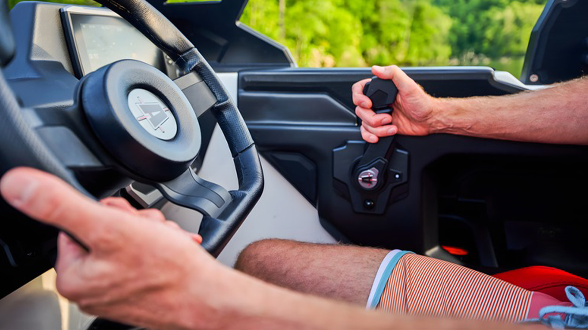 Close-up of a driver's hands on the Axis steering wheel and throttle, red interior and forested hills through the windshield.