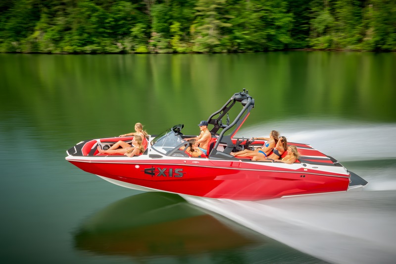 A red Axis A225 runs at speed across a lake with a full crew aboard, green forested hills reflected in the water.