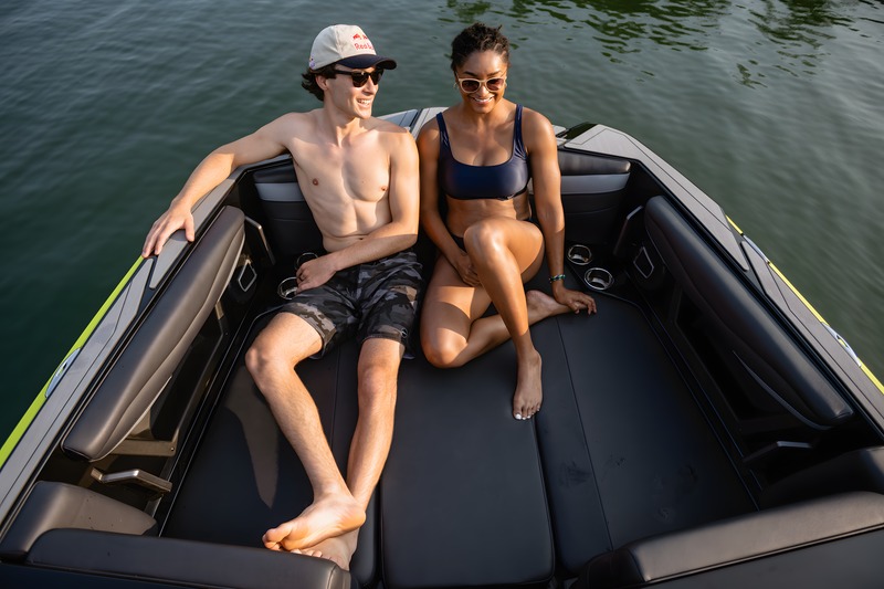 A couple relaxes in the open pickle-fork bow of an Axis A245, black seating with green accents, on calm dark water.