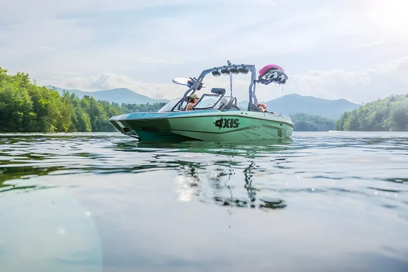 A seafoam-green Axis A200 sits on a calm lake at water level, its reflection mirrored below and forested mountains rising behind.