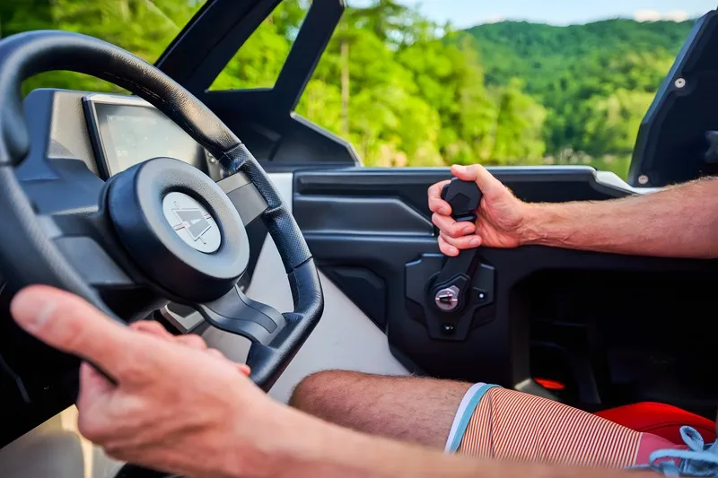 Close-up of a driver's hands on the Axis steering wheel and throttle, red interior and forested hills through the windshield.