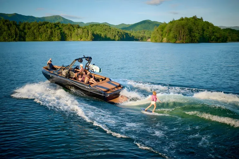 A black Axis T235 tows a young wakesurfer across a mountain lake under a blue sky.