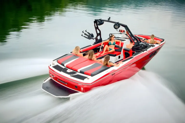 A red-and-white Axis A225 runs across a lake with passengers aboard, motion blur and forested shoreline behind.