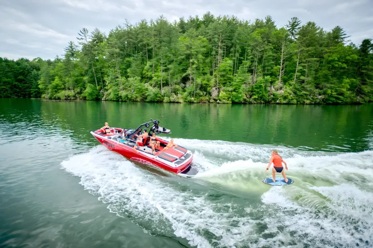 A red Axis A225 tows a wake foiler across a tree-lined green lake, seen from above.