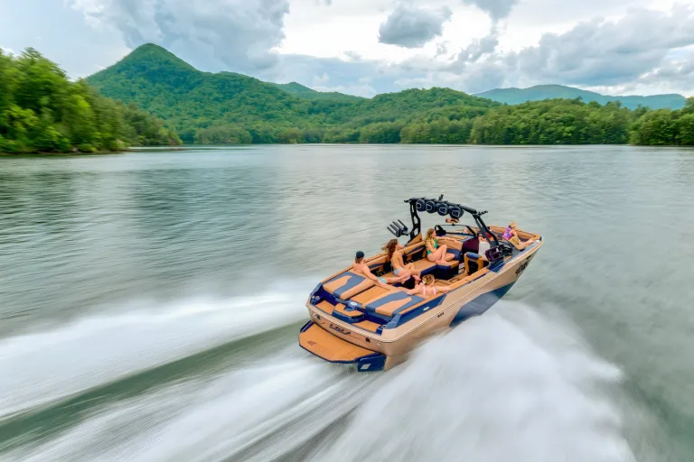 A navy-and-tan Axis A245 runs at speed across a mountain lake, spray trailing and forested peaks behind.