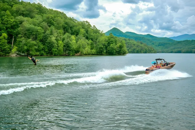 A navy-and-tan Axis A245 tows a wakeboarder across a broad mountain lake under a dramatic cloudy sky.