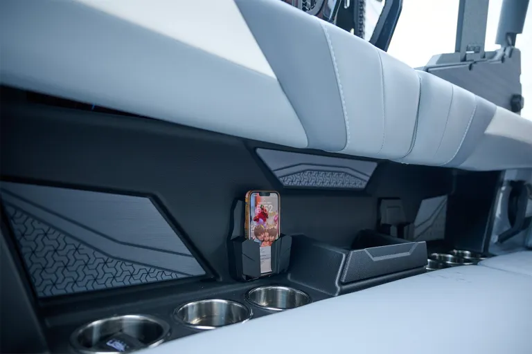 Close-up of a smartphone docked in the Axis T220's seat-side phone holder above a row of stainless cup holders set into the black interior panel.