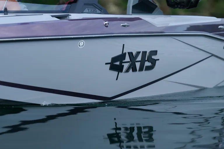 Close-up of the black Axis logo on the white hull of a T220, with the purple accent stripe reflected in the calm water below.