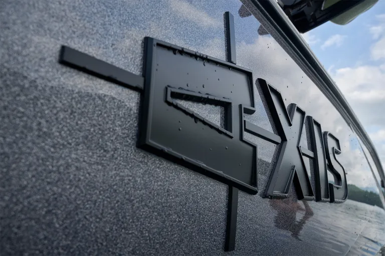 Close-up of the black Axis emblem on the T235's gunmetal metalflake hull, beaded with water droplets and reflecting a cloudy sky.