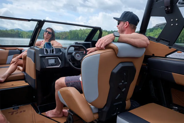 A man in a cap grips the wheel at the Axis T235's helm with its touchscreen dash and stereo, a woman laughing on the seating behind him.