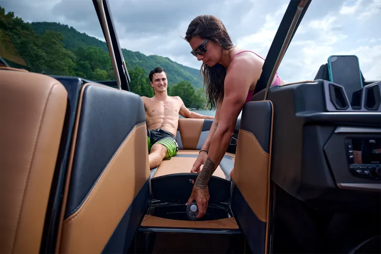 A woman opens the Axis T235's in-floor trash can while a man reclines on the tan seating behind her, the helm and a docked phone in view.